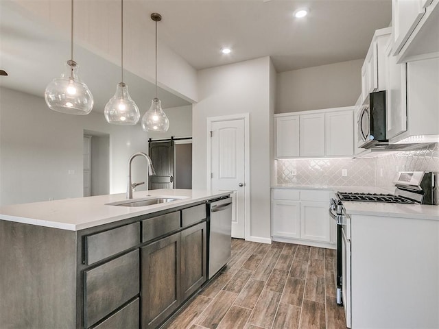 kitchen featuring white cabinetry, sink, stainless steel appliances, a barn door, and a kitchen island with sink