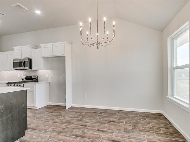 kitchen with backsplash, a chandelier, lofted ceiling, white cabinets, and appliances with stainless steel finishes