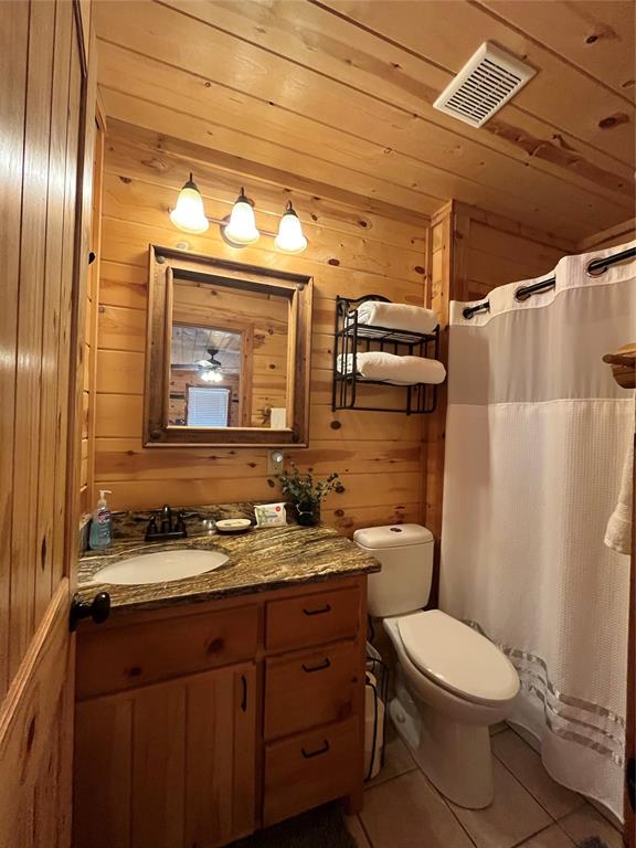 bathroom featuring tile patterned floors, toilet, wooden walls, vanity, and a shower with shower curtain