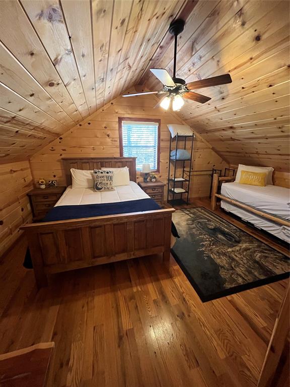 unfurnished bedroom featuring wooden walls, light hardwood / wood-style floors, lofted ceiling, and wood ceiling