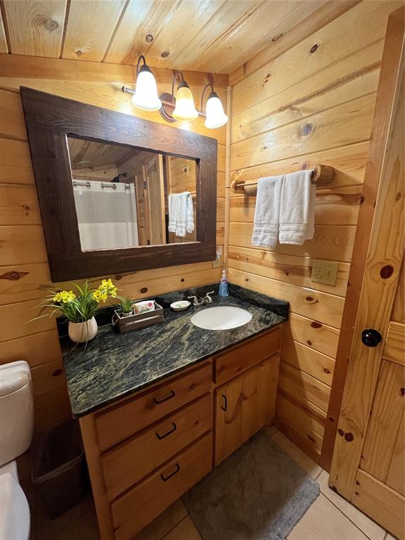 bathroom with vanity, wood walls, wooden ceiling, tile patterned floors, and toilet