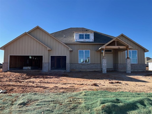 view of front of house with board and batten siding, brick siding, an attached garage, and roof with shingles