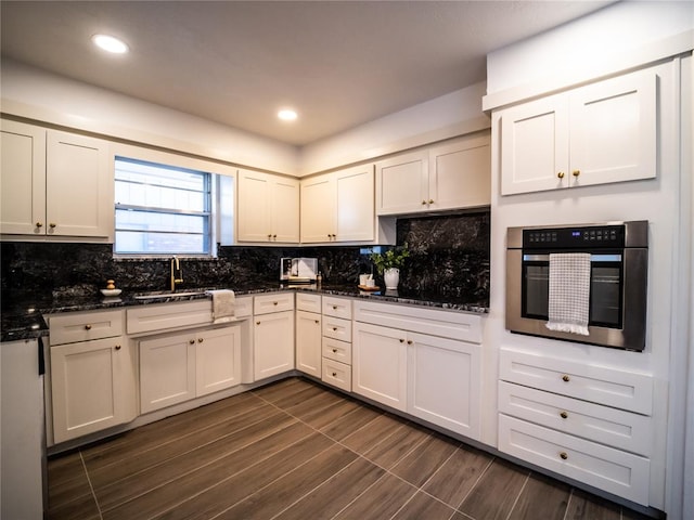 kitchen featuring sink, dark hardwood / wood-style floors, dark stone countertops, black cooktop, and oven