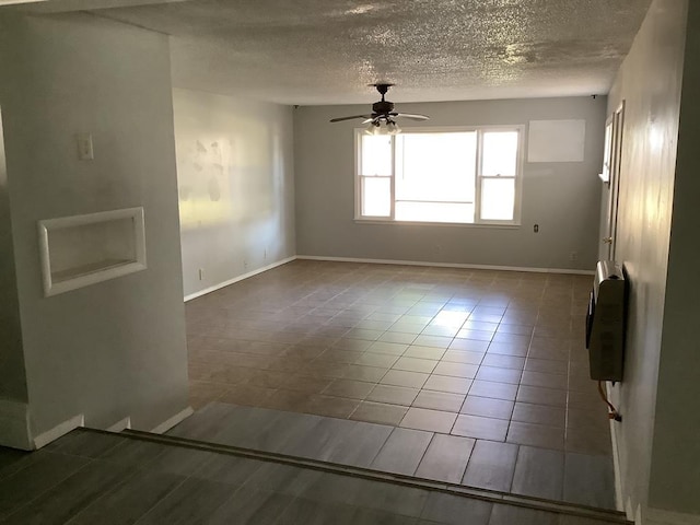 tiled empty room featuring heating unit, ceiling fan, and a textured ceiling