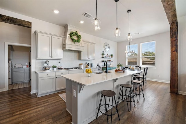 kitchen featuring dark wood-type flooring, a kitchen island with sink, sink, and hanging light fixtures