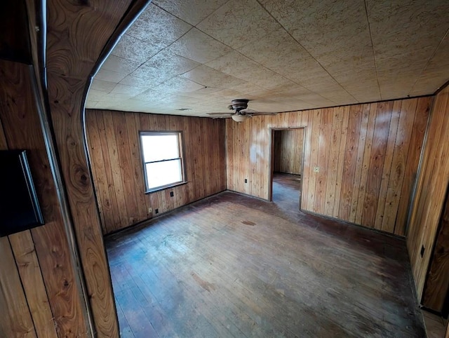 unfurnished room with dark hardwood / wood-style floors, ceiling fan, and wooden walls