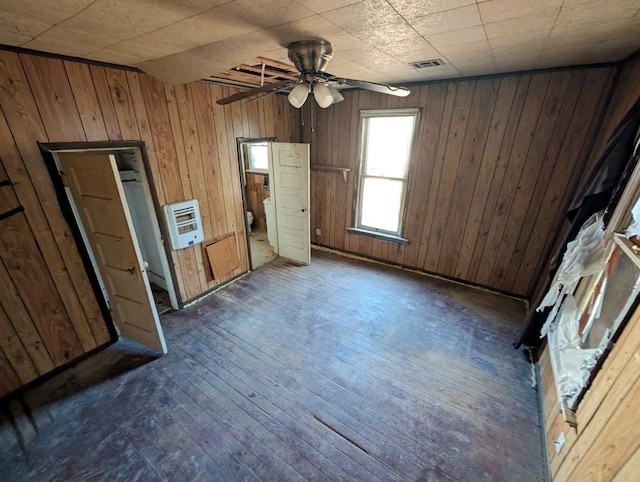 unfurnished bedroom featuring heating unit, wood walls, dark hardwood / wood-style flooring, and ceiling fan