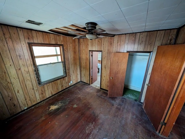 unfurnished bedroom featuring dark hardwood / wood-style floors, ceiling fan, and wooden walls