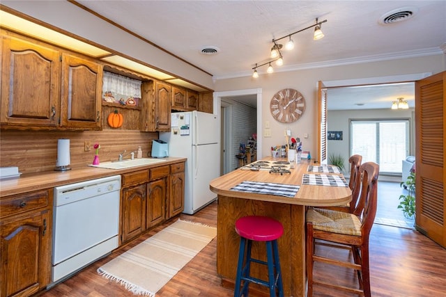 kitchen with sink, hardwood / wood-style floors, white appliances, a breakfast bar area, and a kitchen island