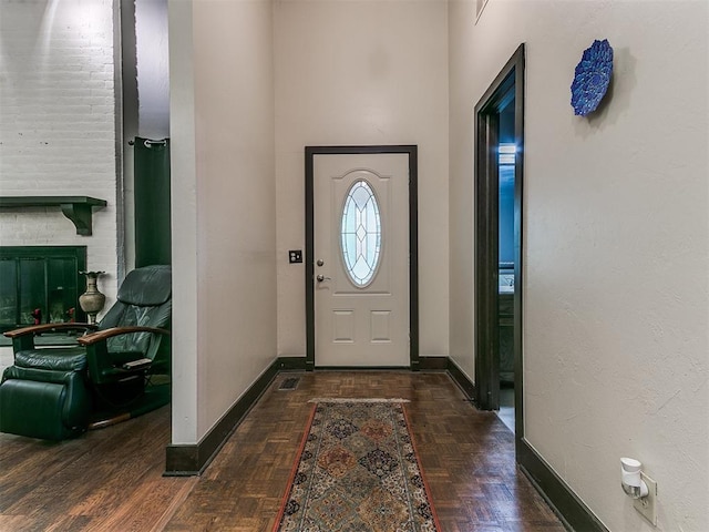 foyer entrance featuring dark parquet flooring and a brick fireplace