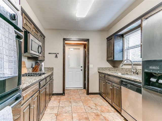 kitchen with light stone countertops, sink, stainless steel appliances, and dark brown cabinets