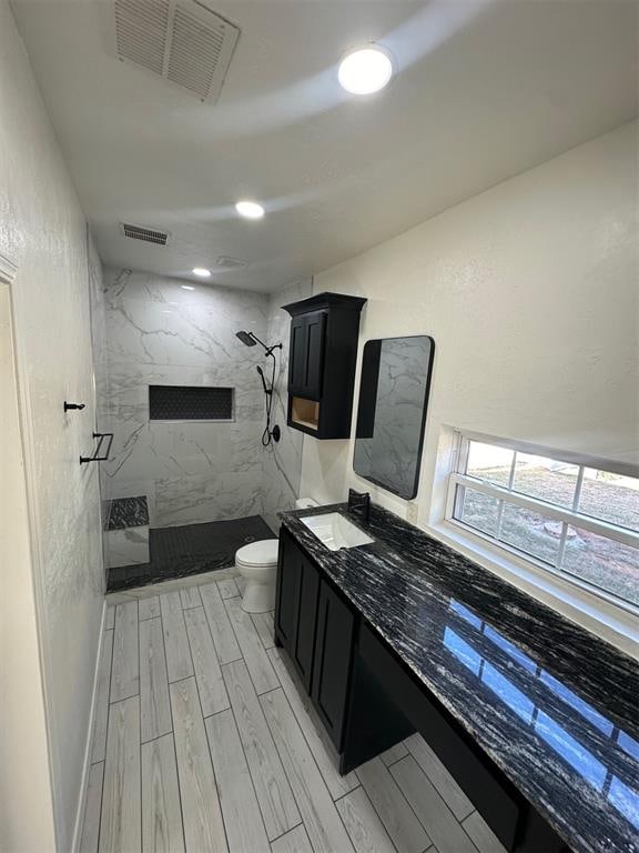 bathroom with tiled shower, vanity, hardwood / wood-style flooring, and toilet