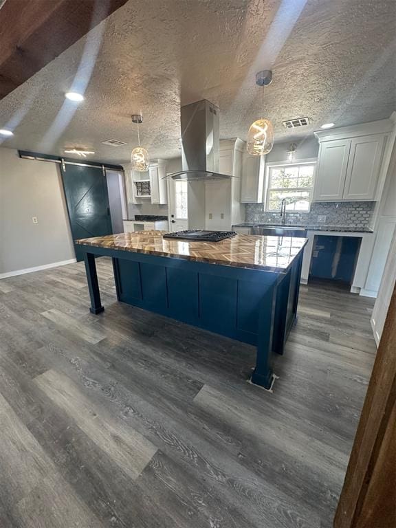 kitchen with white cabinets, a barn door, a kitchen island, and wall chimney range hood