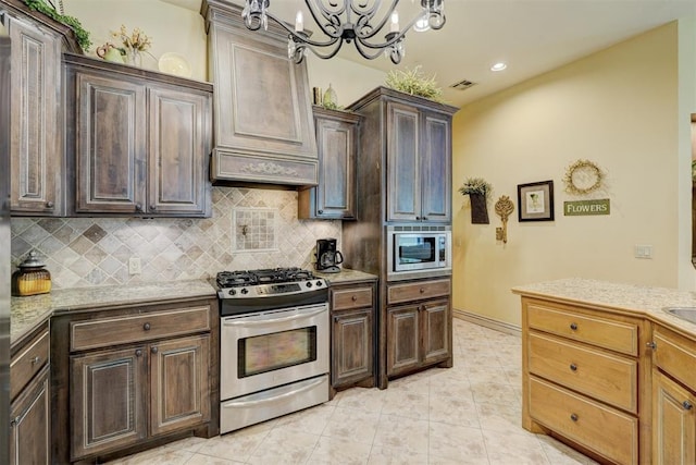 kitchen with backsplash, dark brown cabinetry, stainless steel appliances, light tile patterned floors, and an inviting chandelier