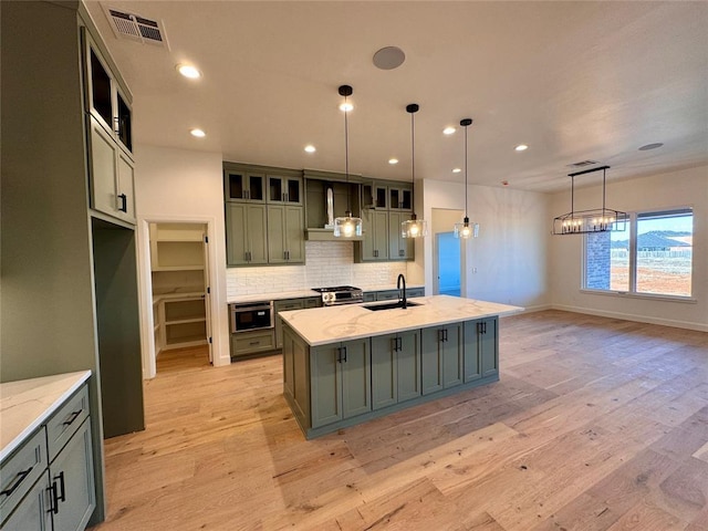 kitchen with a kitchen island with sink, pendant lighting, light stone counters, and light hardwood / wood-style floors