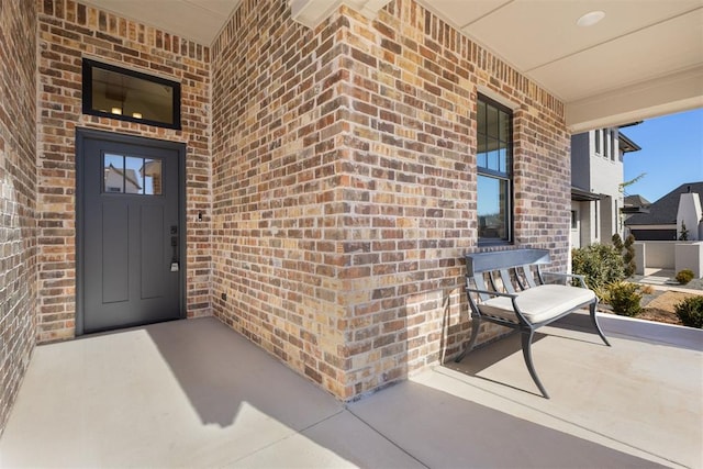 view of exterior entry with brick siding and a porch