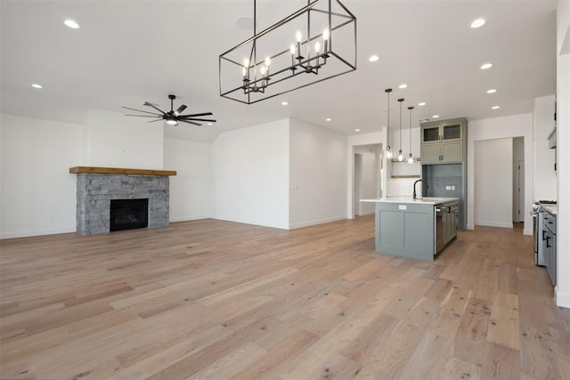 kitchen featuring ceiling fan, an island with sink, light countertops, a stone fireplace, and light wood-style flooring