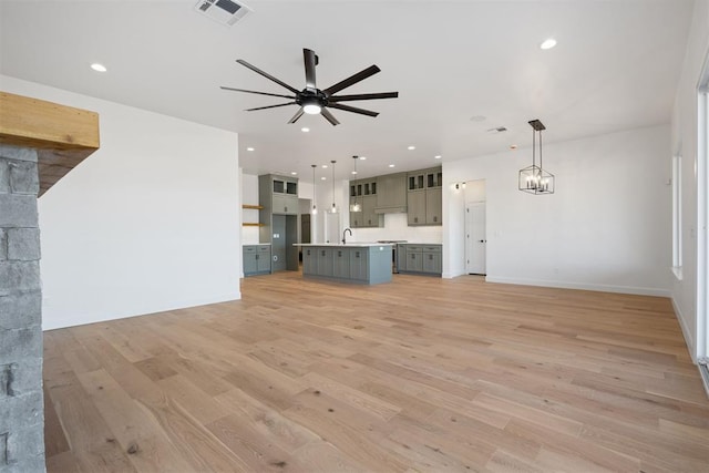 unfurnished living room featuring light wood finished floors, visible vents, baseboards, ceiling fan with notable chandelier, and recessed lighting