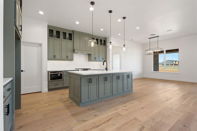 kitchen featuring light wood-style flooring, backsplash, light countertops, and a kitchen island with sink