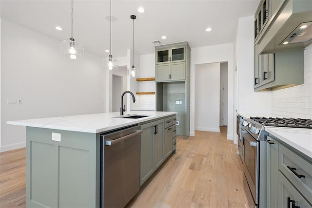 kitchen featuring under cabinet range hood, a center island with sink, light wood-style floors, stainless steel appliances, and a sink