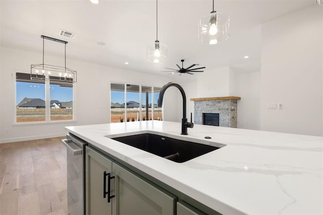 kitchen featuring a sink, light stone countertops, a fireplace, and hanging light fixtures