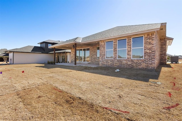 rear view of property with a patio, central AC unit, brick siding, and a shingled roof