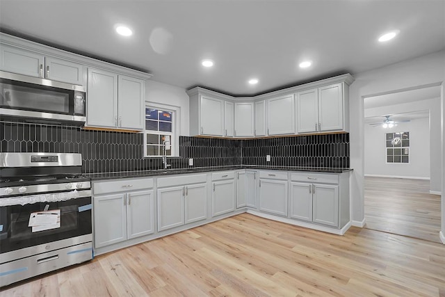 kitchen featuring ceiling fan, backsplash, appliances with stainless steel finishes, white cabinets, and light wood-type flooring