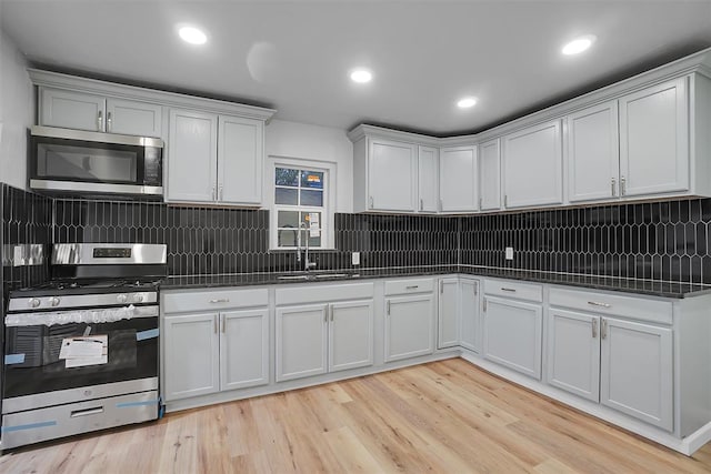 kitchen with sink, white cabinets, light wood-type flooring, and appliances with stainless steel finishes