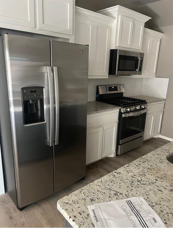 kitchen with light stone countertops, white cabinets, stainless steel appliances, and hardwood / wood-style flooring