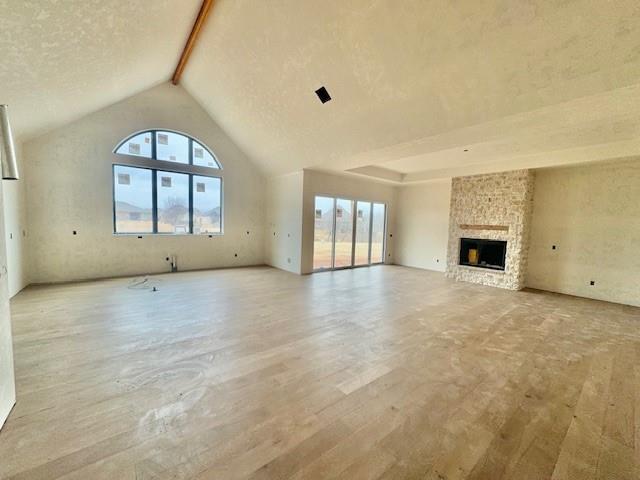 unfurnished living room with plenty of natural light, beam ceiling, a fireplace, and high vaulted ceiling