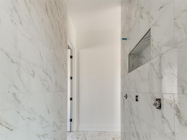 bathroom with marble finish floor, a tile shower, and baseboards