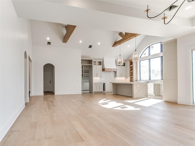 unfurnished living room with arched walkways, visible vents, high vaulted ceiling, light wood-type flooring, and beamed ceiling