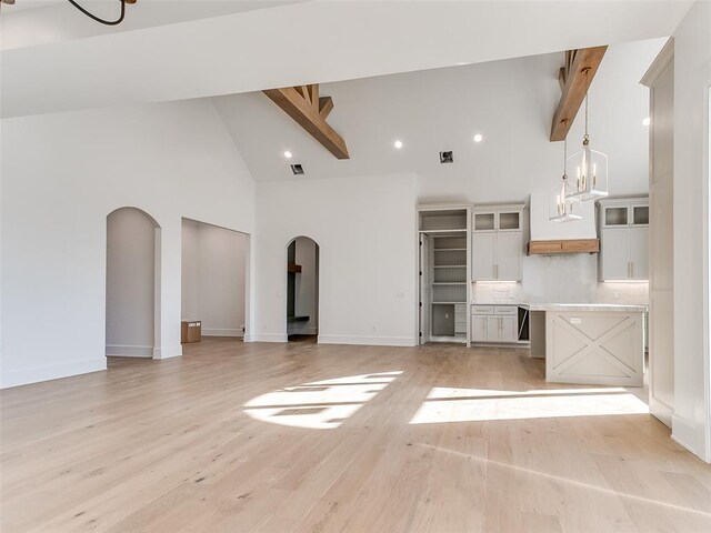 kitchen featuring arched walkways, light wood finished floors, backsplash, white cabinets, and beamed ceiling