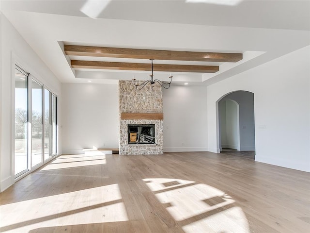 unfurnished living room with light wood finished floors, arched walkways, beamed ceiling, a fireplace, and a notable chandelier