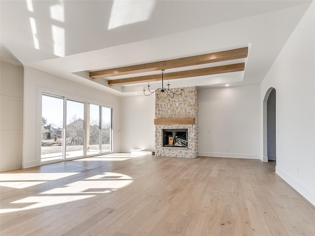 unfurnished living room with arched walkways, light wood-style flooring, a stone fireplace, beamed ceiling, and baseboards