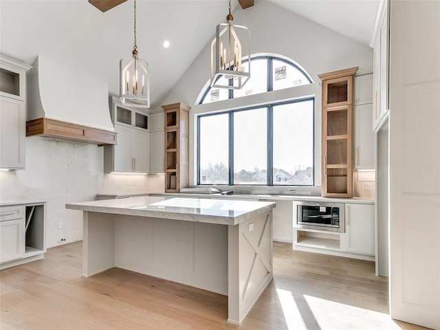 kitchen featuring light wood finished floors, tasteful backsplash, stainless steel microwave, a kitchen island, and a chandelier