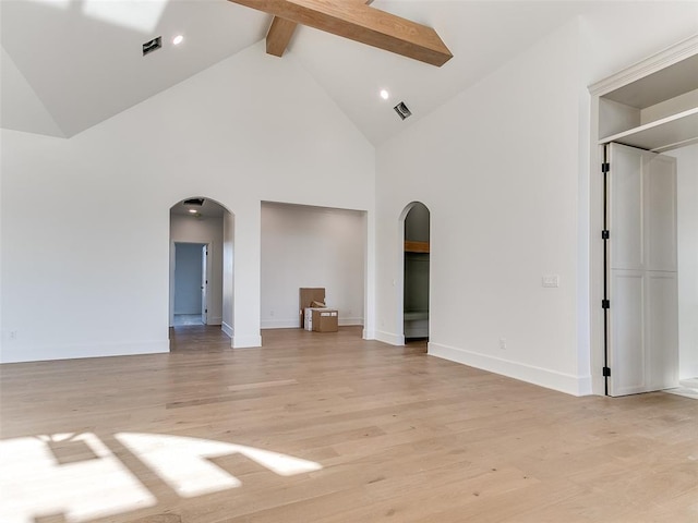 empty room featuring arched walkways, baseboards, beam ceiling, and light wood-style floors