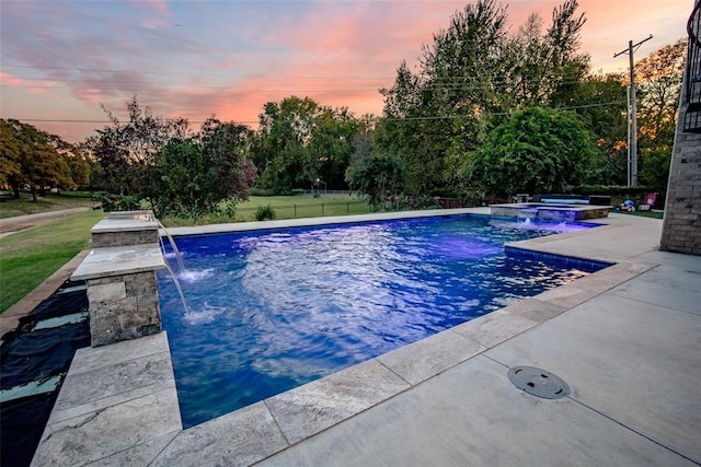 pool at dusk with pool water feature and an in ground hot tub