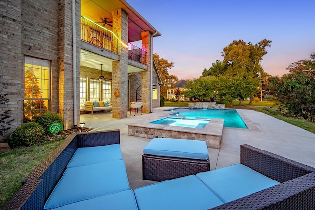 pool at dusk with ceiling fan, an outdoor living space, a patio, and an in ground hot tub