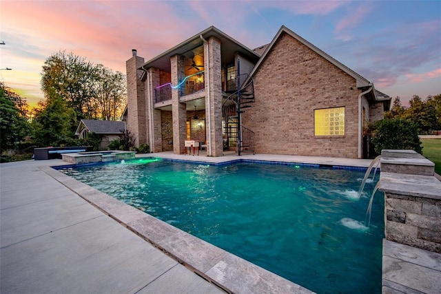 pool at dusk with pool water feature, a patio area, and an in ground hot tub