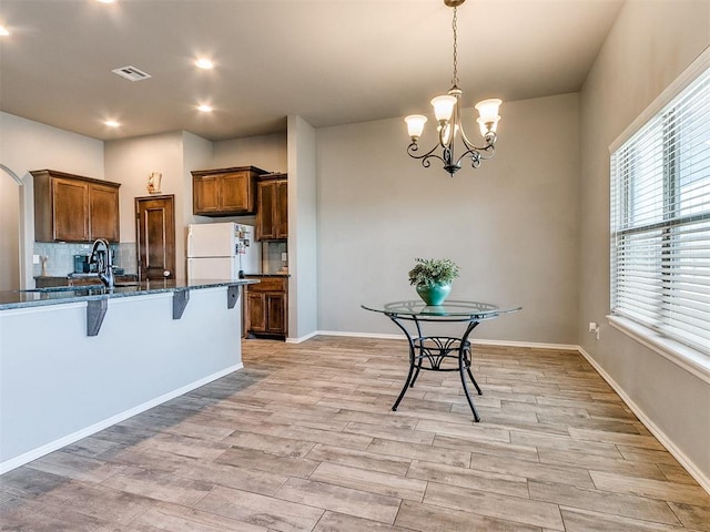 kitchen featuring decorative light fixtures, white refrigerator, a kitchen bar, and light wood-type flooring