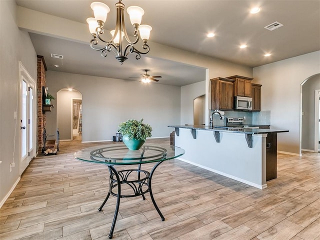 kitchen with a kitchen bar, appliances with stainless steel finishes, light wood-type flooring, and decorative light fixtures