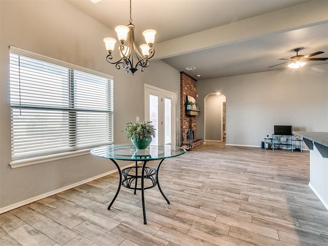 dining room featuring a brick fireplace, ceiling fan with notable chandelier, light hardwood / wood-style floors, and lofted ceiling with beams