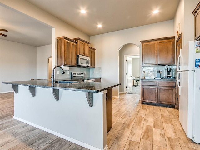 kitchen with dark stone counters, sink, stainless steel appliances, and light hardwood / wood-style floors