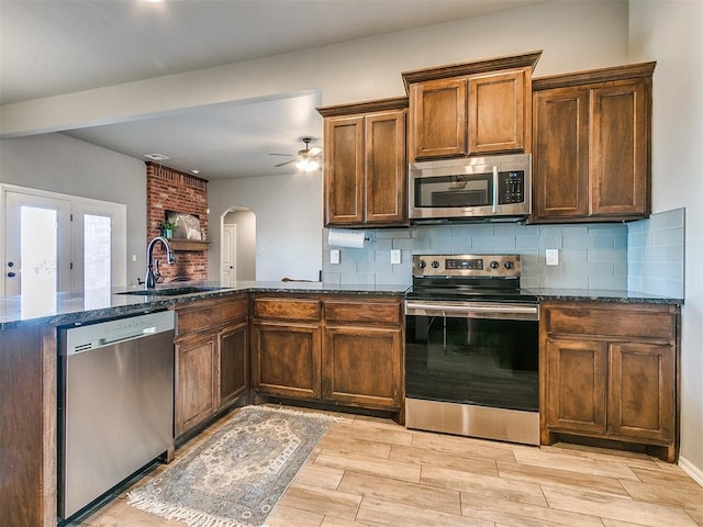 kitchen with appliances with stainless steel finishes, light wood-type flooring, ceiling fan, sink, and dark stone countertops