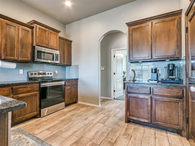 kitchen featuring backsplash, dark stone counters, stainless steel appliances, and light wood-type flooring