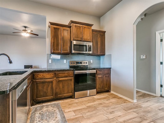 kitchen with sink, stainless steel appliances, tasteful backsplash, dark stone countertops, and kitchen peninsula