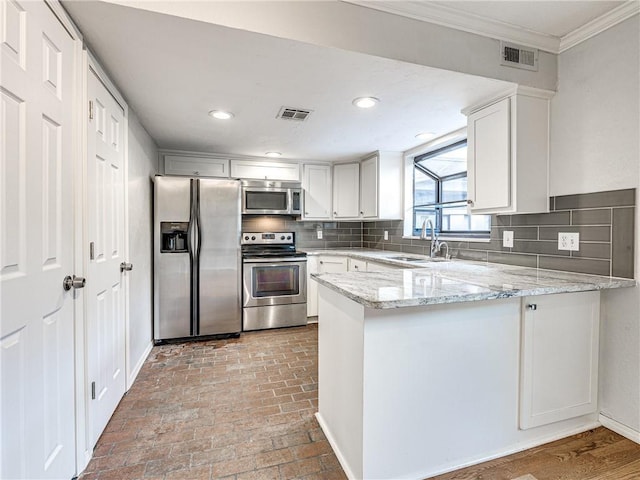 kitchen with light stone countertops, white cabinetry, sink, stainless steel appliances, and kitchen peninsula