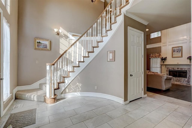 stairway with wood-type flooring, a towering ceiling, a fireplace, and ornamental molding