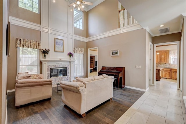 living room featuring ceiling fan, crown molding, a towering ceiling, a fireplace, and hardwood / wood-style flooring